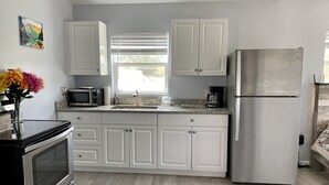 A modern kitchen with white cabinets, stainless steel appliances, and a wooden floor.