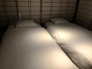A room with two beds, each with a pillow and a blanket. The room has a traditional Japanese shoji screen design on the walls.