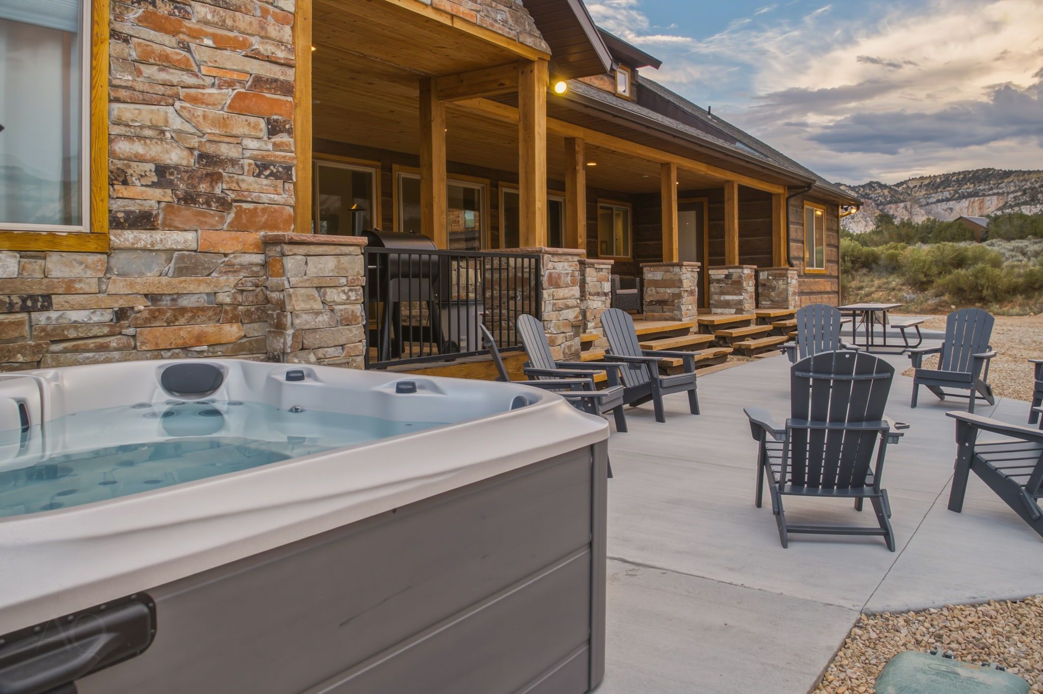 A hot tub and outdoor seating area with Adirondack chairs, a stone wall, and a wooden deck.