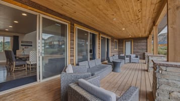 A covered outdoor seating area with sofas and chairs, wooden flooring, and a stone wall.