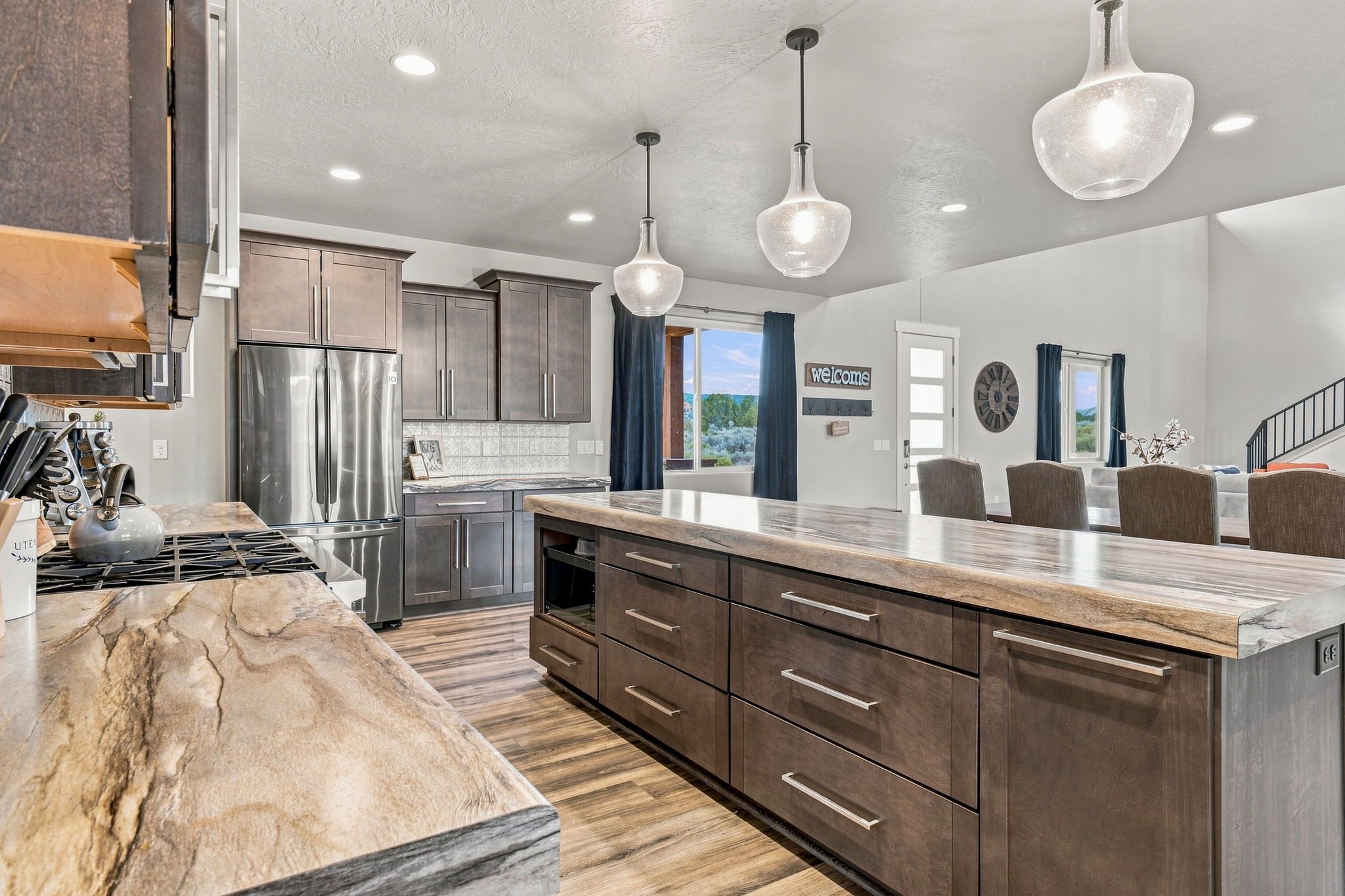 A modern kitchen with a large island, stainless steel appliances, and pendant lighting.