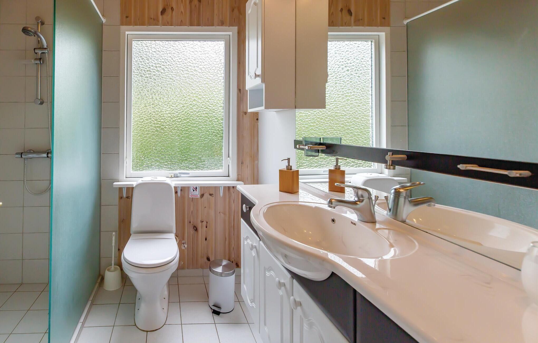 A modern bathroom with a toilet, bidet, sink, and shower. There is a window providing natural light and a view of greenery outside.