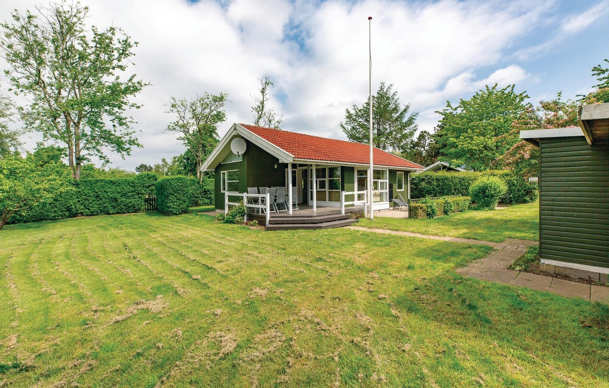 A small house with a red roof, a porch with chairs, and a satellite dish.