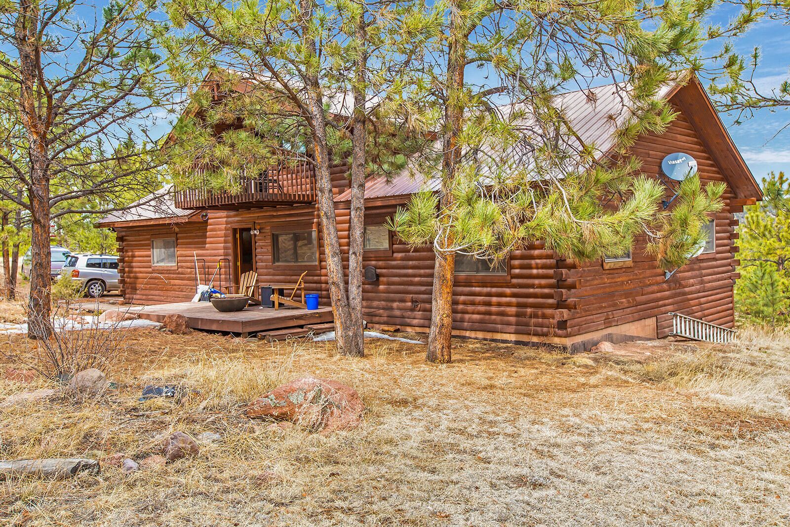 A log cabin with a porch, a small deck, and a satellite dish.