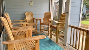 A covered porch with wooden Adirondack chairs and a small table, a blue rug, and a sign that reads "Work like a Captain, Play like a Pirate." - Hawk's Nest Boyette Condo 1D: Centrally located with Pool (Ocracoke)