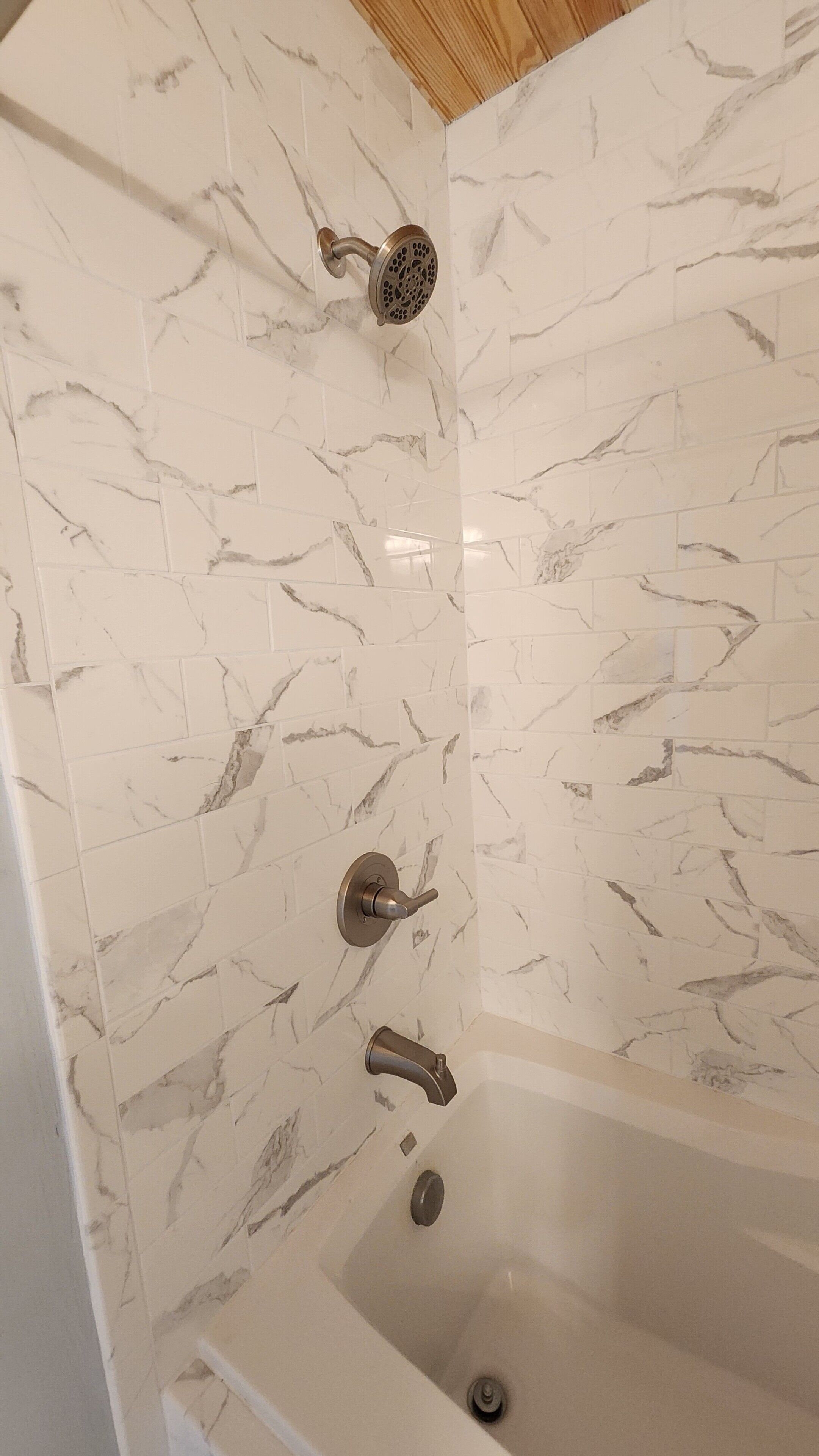 A bathroom with a marble wall, a bathtub, and a shower with a handheld showerhead.