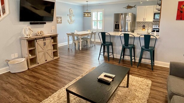 A modern living room with a flat-screen TV, a wooden cabinet, and a dining area with chairs and a table. - Hawk's Nest Boyette Condo 1D: Centrally located with Pool (Ocracoke)