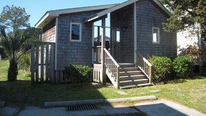 A small, single-story house with a porch and a set of stairs leading to the entrance. - Hawk's Nest Boyette Condo 1D: Centrally located with Pool (Ocracoke)
