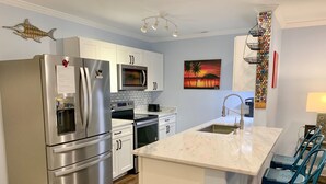 A modern kitchen with stainless steel appliances, white cabinetry, and a marble island. - Hawk's Nest Boyette Condo 1D: Centrally located with Pool (Ocracoke)