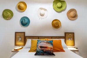 A bed with a white pillow and an orange pillow, two nightstands, and a wall with seven hats. - Casa Babi (Cienfuegos)