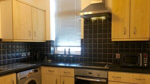 Une cuisine compacte avec des meubles en bois, un four encastré, un four à micro-ondes et un lave-linge.