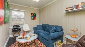 A living room with a blue sofa, a round coffee table, a white chair, a colorful rug, a bookshelf, and a painting on the wall. - Luxurious 1BR Located Near Downtown & Hospital (Winston-Salem)