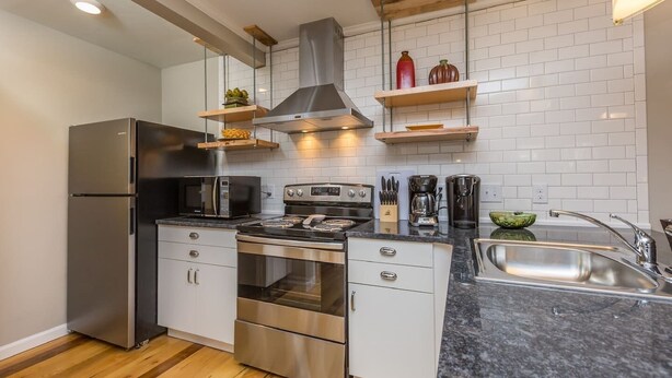 A modern kitchen with stainless steel appliances, a wooden floor, and white subway tiles. - Luxurious 1BR Located Near Downtown & Hospital (Winston-Salem)