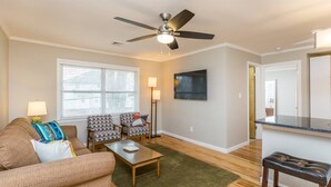 A living room with a ceiling fan, a TV, a sofa, two armchairs, a coffee table, and a bench. - Luxurious 1BR Located Near Downtown & Hospital (Winston-Salem)