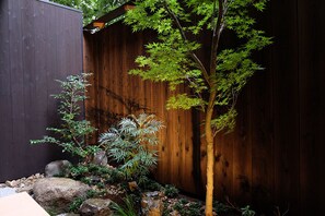 A small garden with a wooden fence, a tree, and various plants.