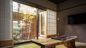 Una habitación japonesa tradicional con suelo de tatami, una mesa de madera, puertas correderas y un televisor en la pared.