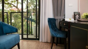 A modern room with a blue sofa, a desk with a chair, a potted plant, and a view through a glass door. - Marina Hotel (Hanoi)