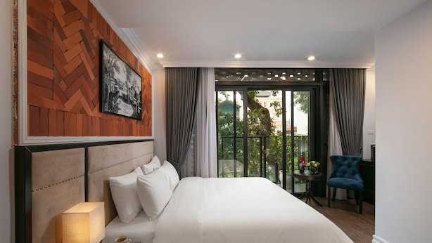 A hotel room with a large bed, a nightstand with a lamp, a phone, and a view of a balcony with a chair. - Marina Hotel (Hanoi)