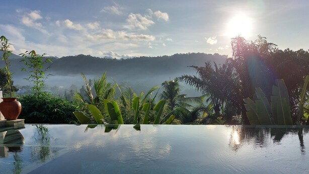 Une piscine paisible aux eaux limpides, bordée d’une végétation tropicale luxuriante et dominée par une chaîne de montagnes.