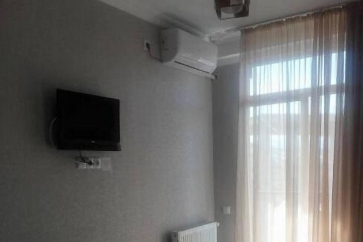 A hotel room with a bed, a TV mounted on the wall, a window with curtains, and a radiator.
