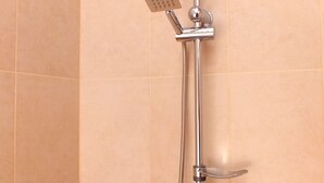 A shower with a handheld showerhead and a fixed showerhead, mounted on a wall with decorative tiles. - Hotel Petre Palace (Tbilisi)