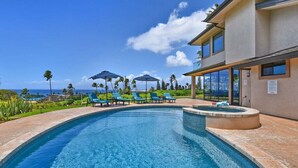 A swimming pool with lounge chairs and umbrellas, surrounded by palm trees and a building with large windows.