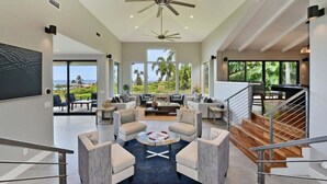 A spacious living area with a large window offering a view of the outdoors, a ceiling fan, and a staircase leading to another level.