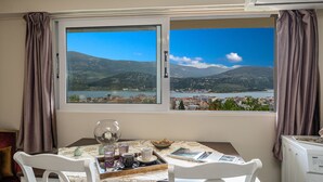 Una habitación con una mesa puesta para dos, vistas a un lago y montañas, y una ventana con cortinas.