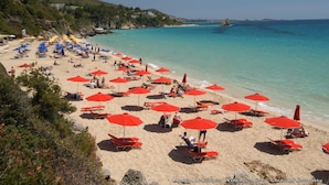 Una playa con numerosas sombrillas rojas y tumbonas.