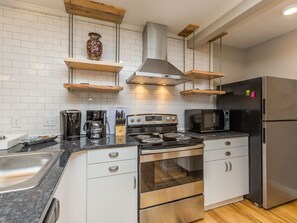 Een moderne keuken met witte kastjes, roestvrijstalen apparatuur en houten planken.