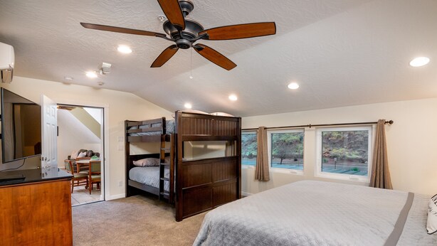 Quarto com uma cama grande, um ventilador de teto, uma escrivaninha com cadeira e uma beliche.