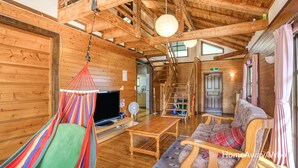 A cozy cabin interior with a hammock, wooden furniture, and a staircase leading to a loft.