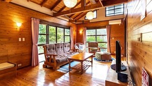 A cozy cabin interior with wooden walls, a sofa, chairs, a table, and a television.