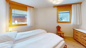 Una camera da letto con due letti, testiere in legno, una cassettiera e tende alle finestre.