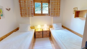 Een slaapkamer met twee eenpersoonsbedden, een houten nachtkastje met een lamp, en een raam met oranje gordijnen.