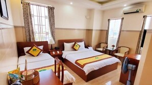 A hotel room with two beds, a wooden desk, a fan, and a window with curtains. - Thanh An Hotel (Ho Chi Minh City)