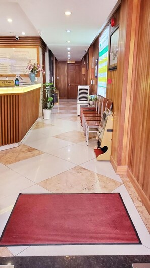 Un hall d’hôtel comprenant un comptoir d’accueil, un tapis rouge, un espace détente avec des fauteuils et un climatiseur fixé au mur.