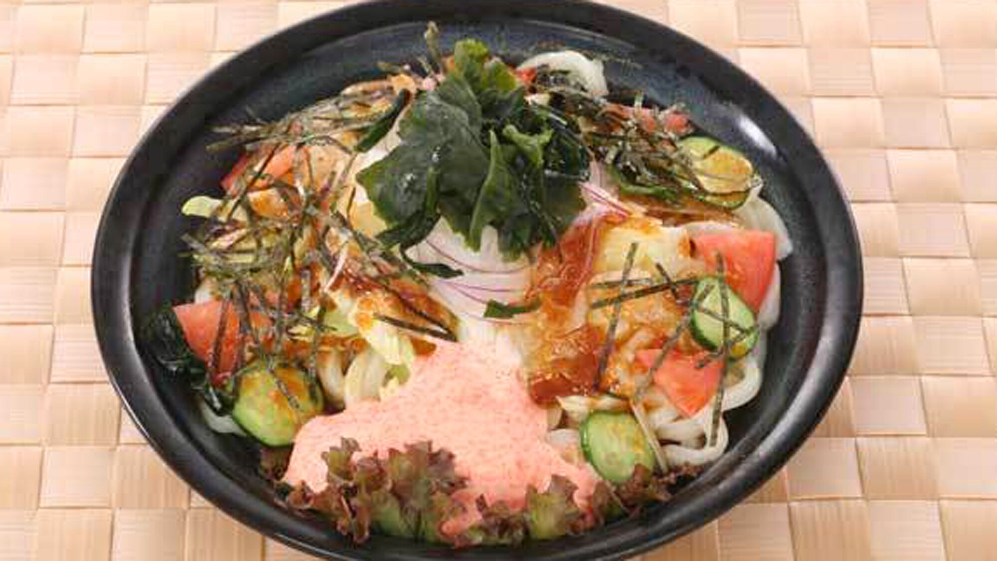 A black plate with various vegetables and a pink sauce on a woven mat.