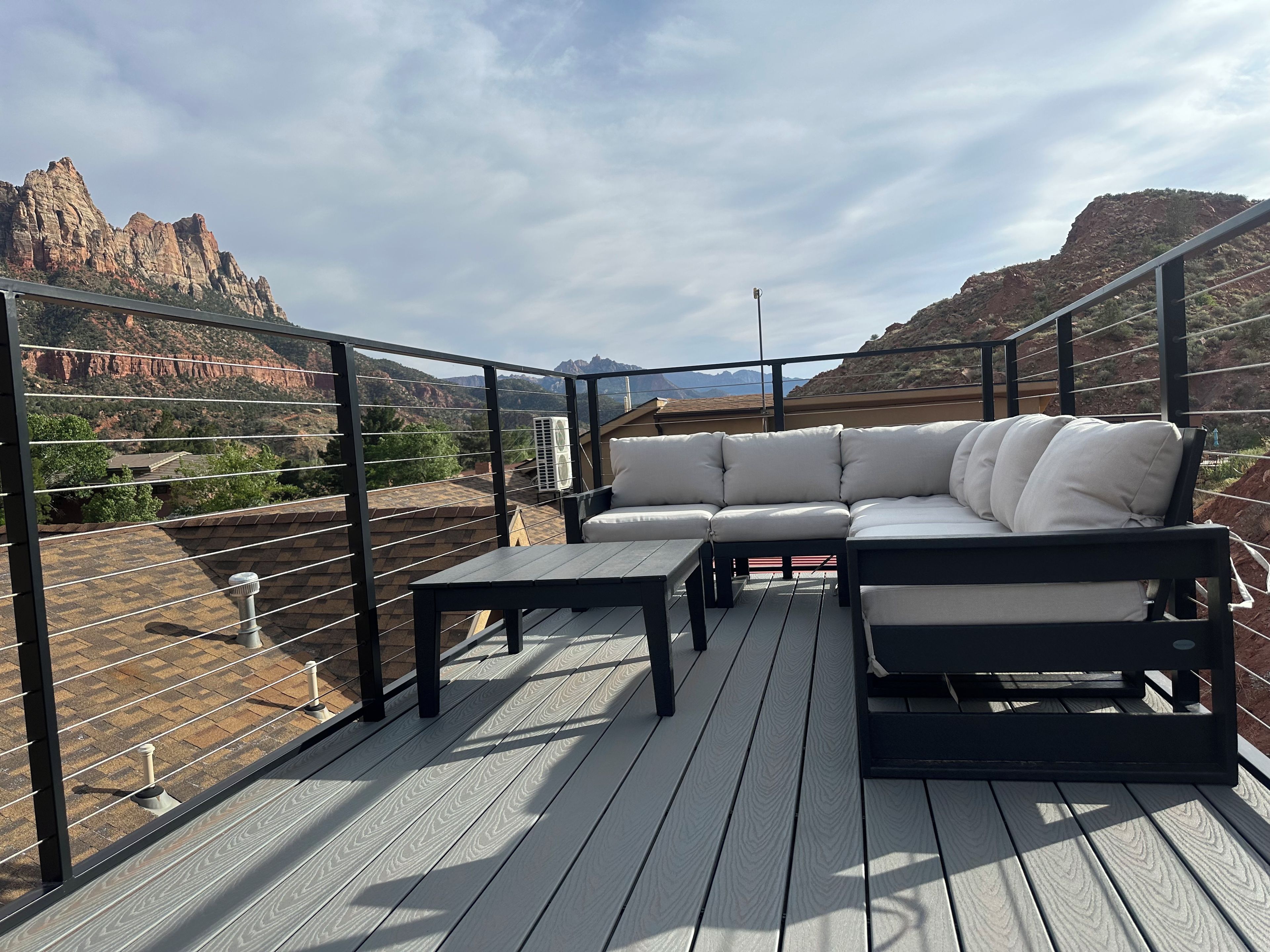 Varanda externa com sofá modular e mesa, com vista para uma paisagem montanhosa.