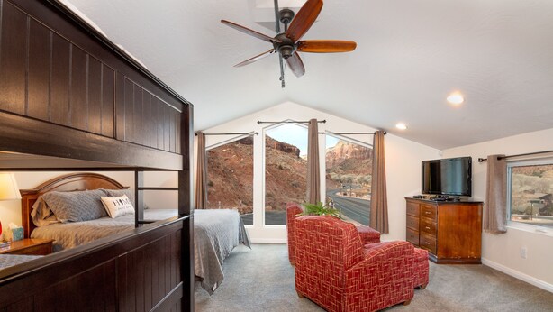 A bedroom with a bed, a red patterned chair, a TV, and a large window offering a view of a mountainous landscape. - Apartment #1 GREAT LOCATION Zion National Park entrance as close as you can get! (Springdale)