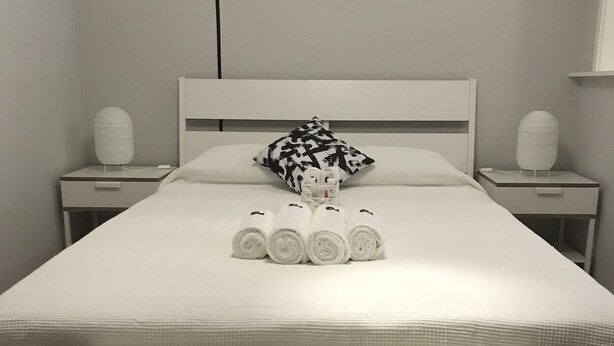A neatly made bed with rolled towels, a pillow with a black and white pattern, and a wall decoration of an owl on a branch. - H.ö.H (Porto)