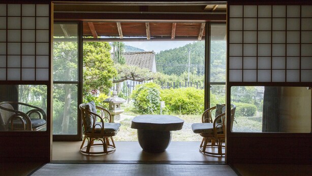 A traditional Japanese room with tatami flooring, a shoji screen, and a view of a garden with a stone lantern.