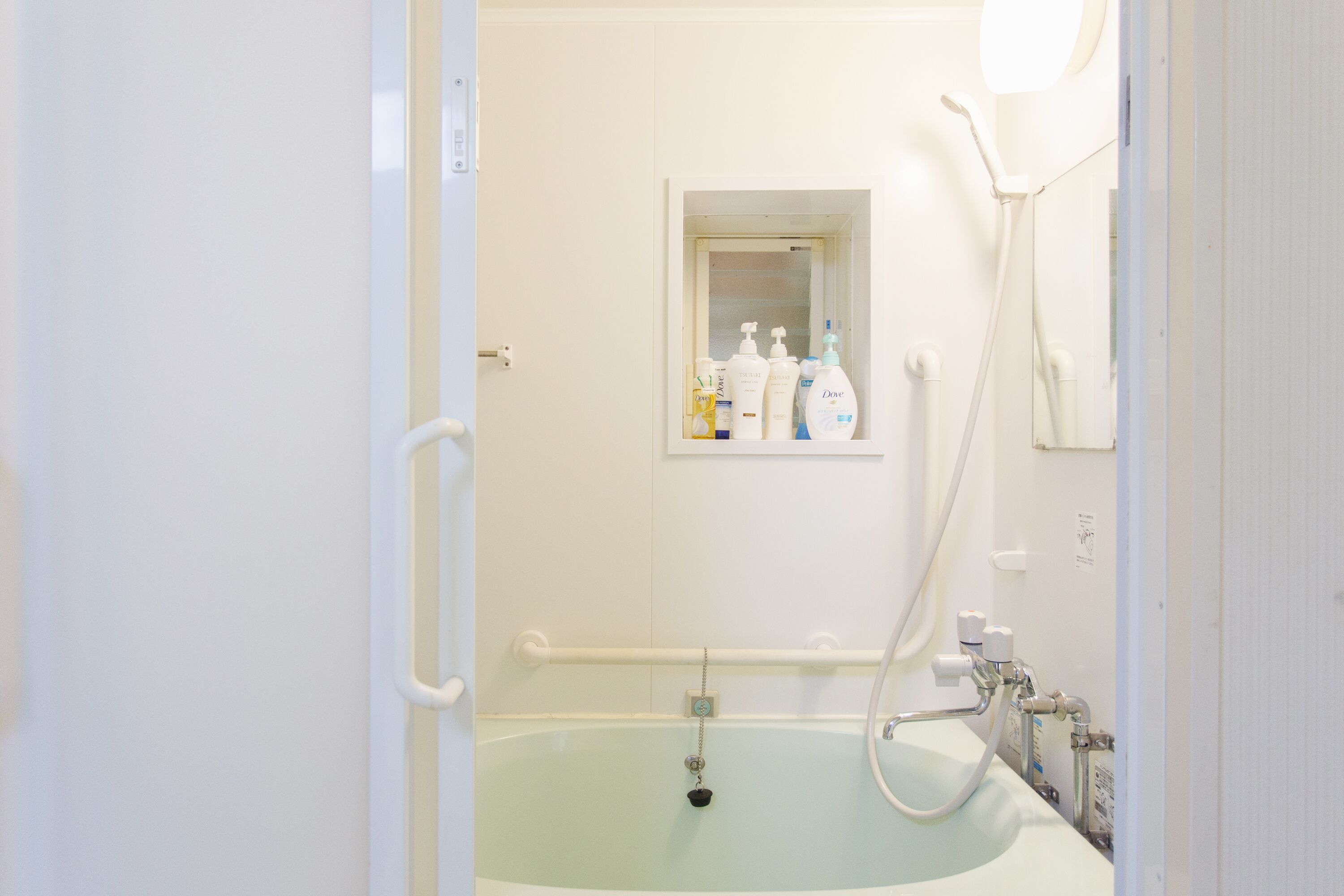Ein Badezimmer mit einer Badewanne, einer Haltestange, einem Fenster mit Toilettenartikeln und einer Dusche.