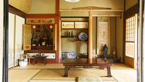 A traditional Japanese room with tatami flooring, a low wooden table, and various decorative items including a blue and white ceramic plate, a statue, and a hanging scroll.