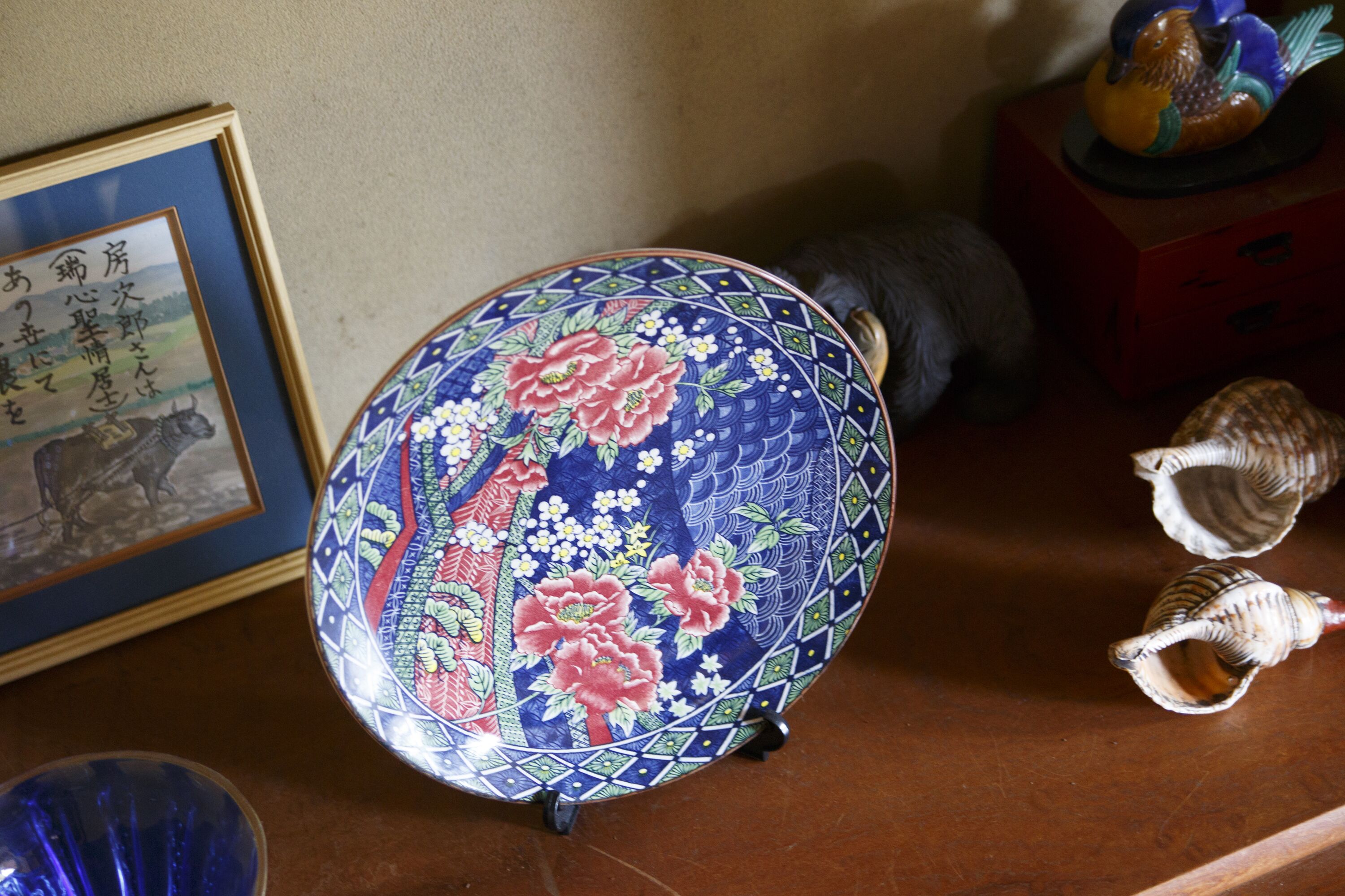 A decorative plate with floral patterns, a framed picture, and small figurines on a wooden surface.