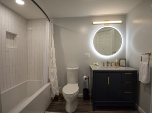 A bathroom with a bathtub, toilet, vanity with a mirror, and a towel rack.