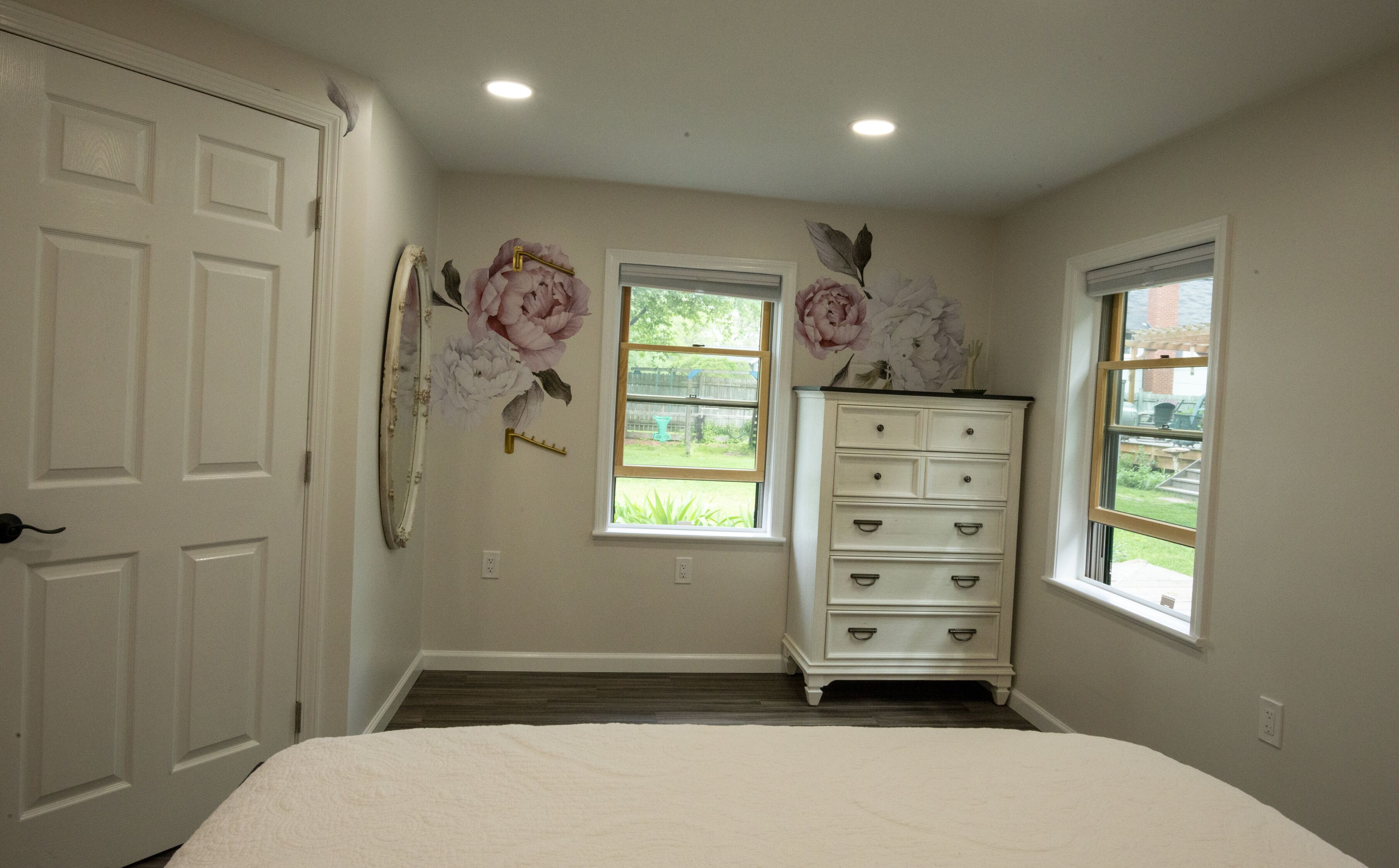 A bedroom with a bed, a dresser, two windows, and a door.
