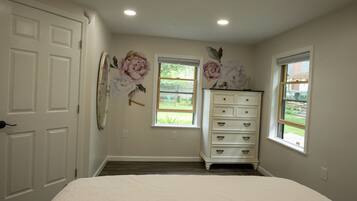 A bedroom with a bed, a dresser, two windows, and a door.