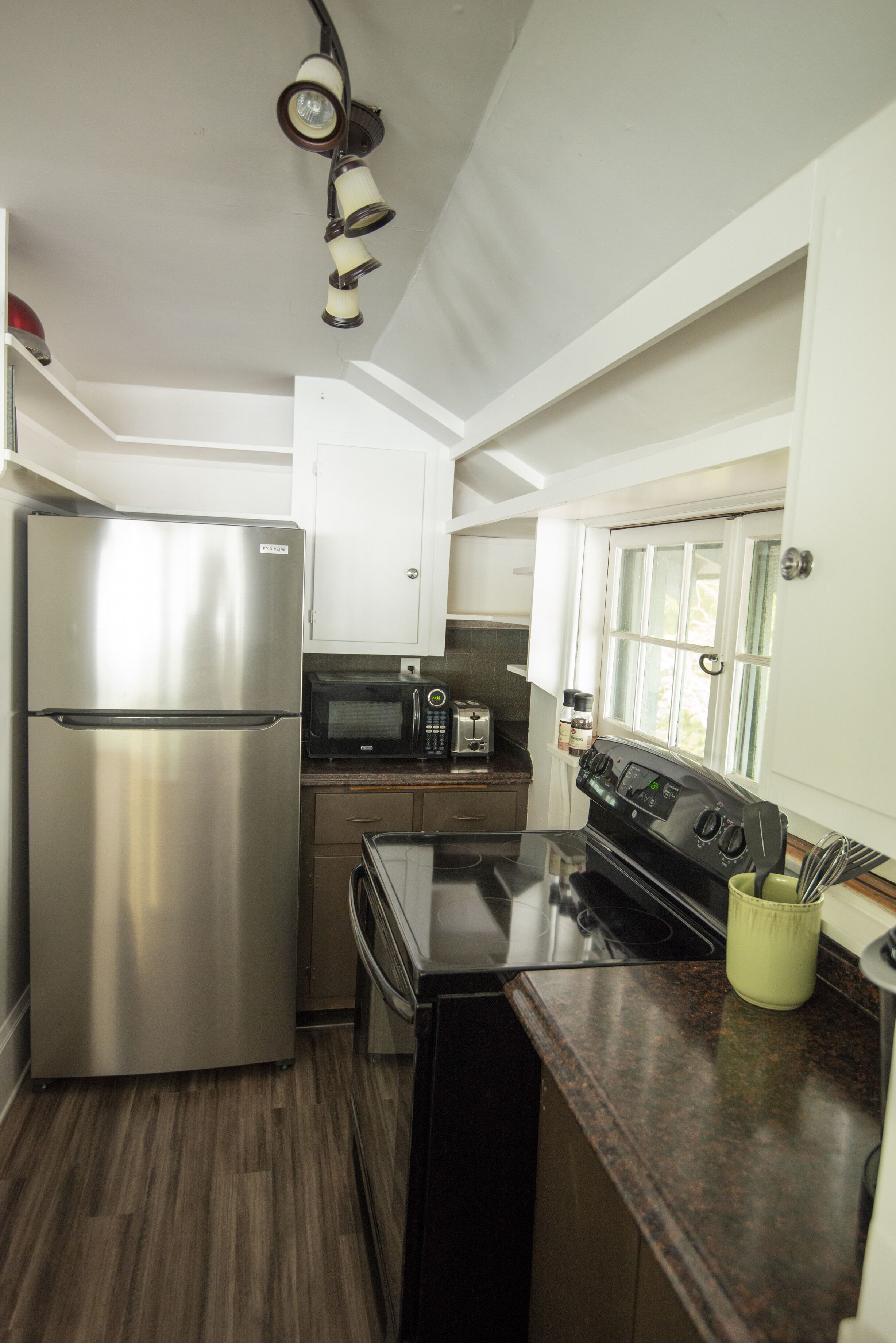 A compact kitchen with a stainless steel refrigerator, a microwave, a toaster, and a stove.