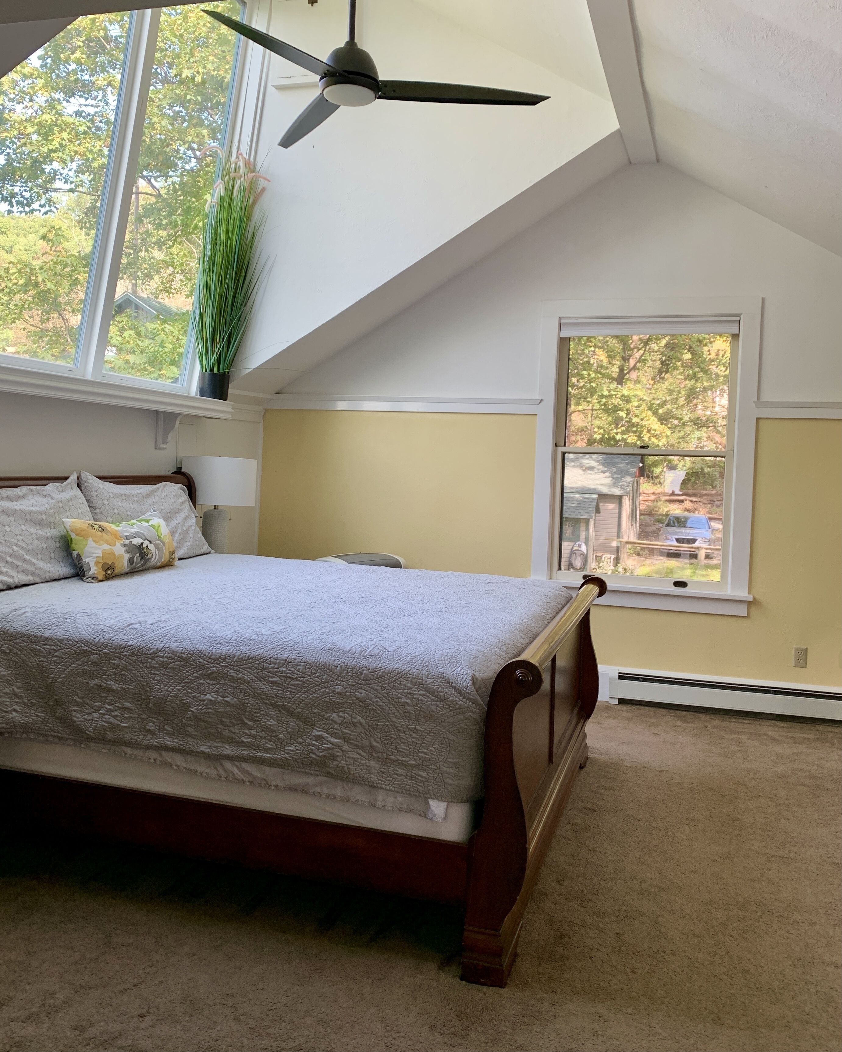 A bedroom with a bed, a ceiling fan, a window with a view, and a potted plant.